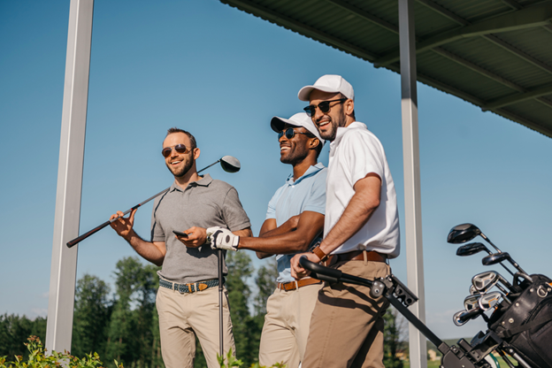 Three male friends on a driving range smiling and laughing in the sun