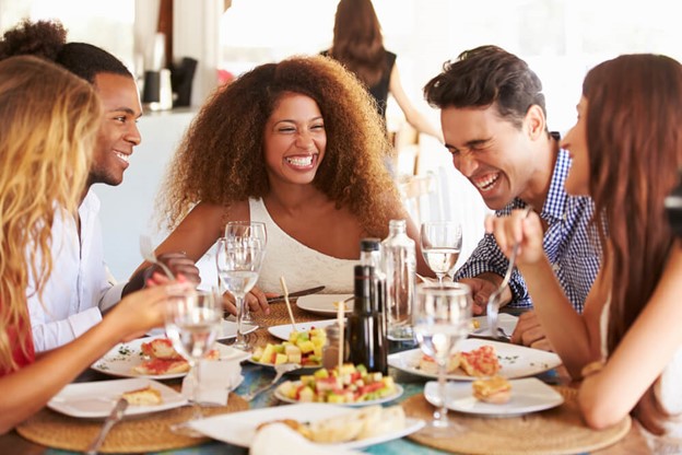 Group of friends eating at a table laughing, smiling and having a good time.